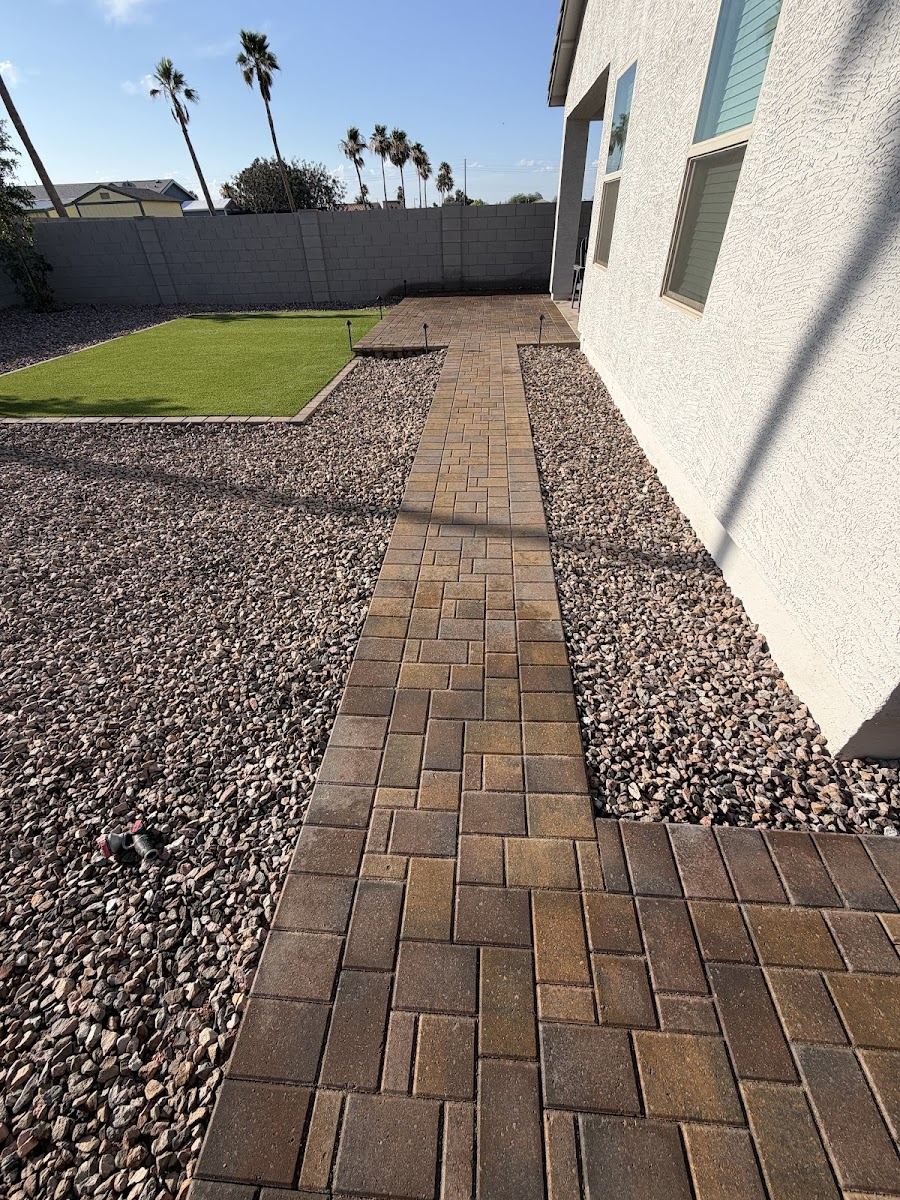 Paver walkway running through rock beds toward a turf patch