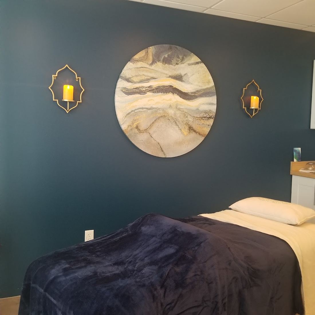 A dark teal treatment room with round gold art and wall sconces