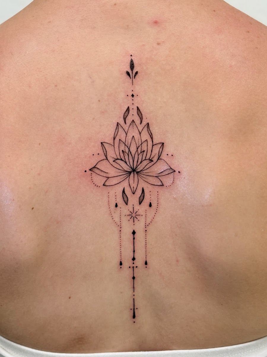 Fine line lotus ornamental tattoo along the spine