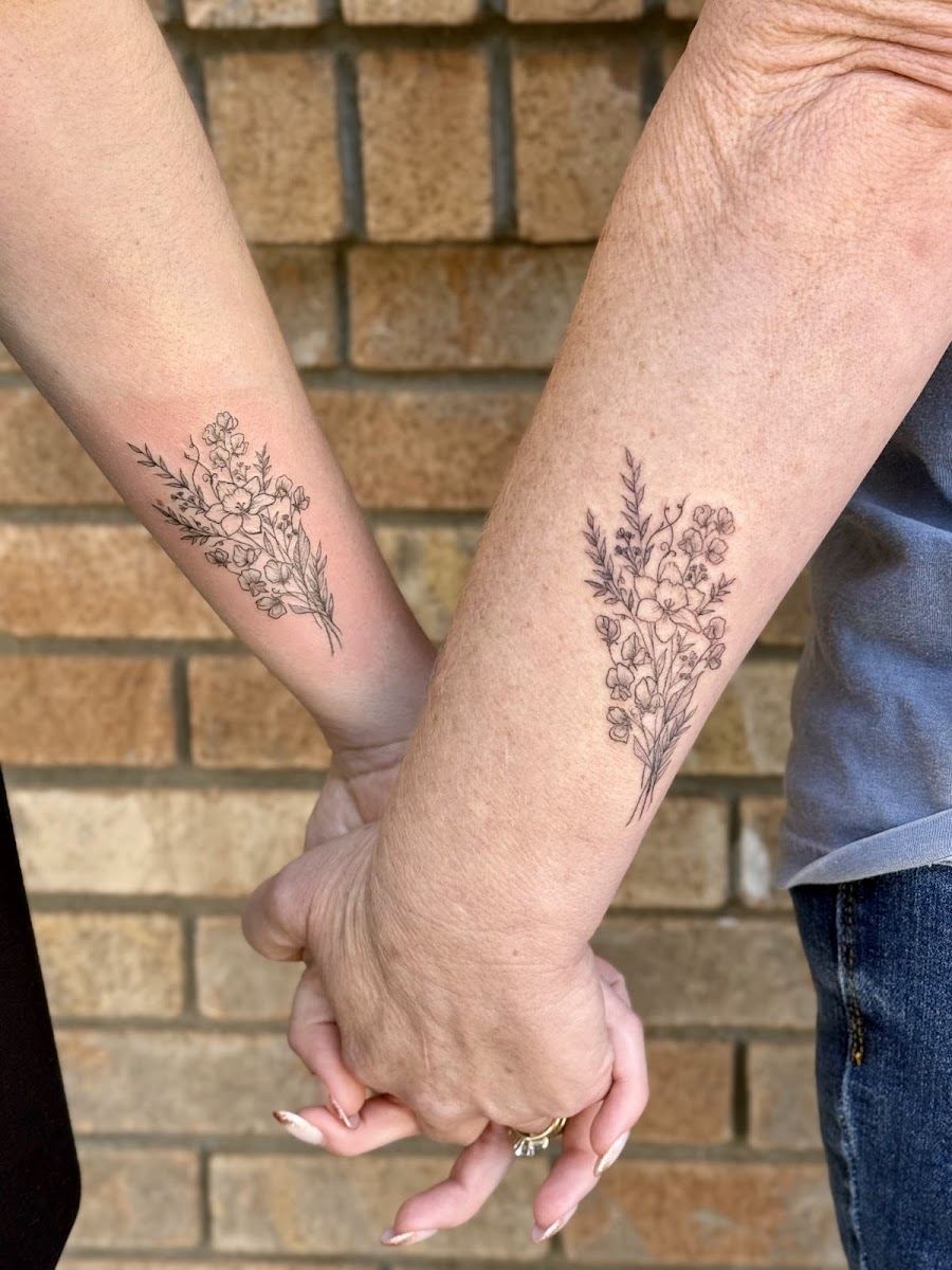 Two people holding hands with matching wildflower bouquet tattoos on their forearms