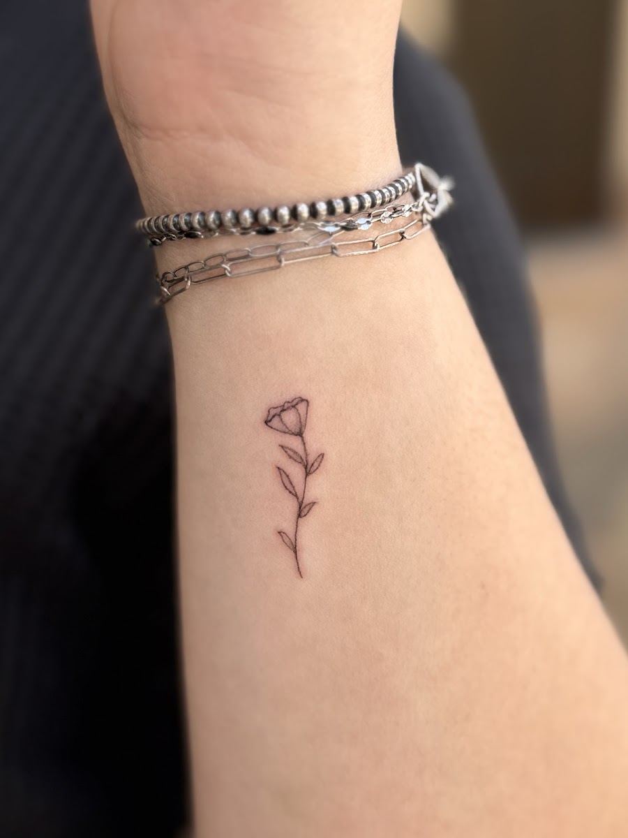 Single stem flower tattoo on an inner wrist below silver bracelets