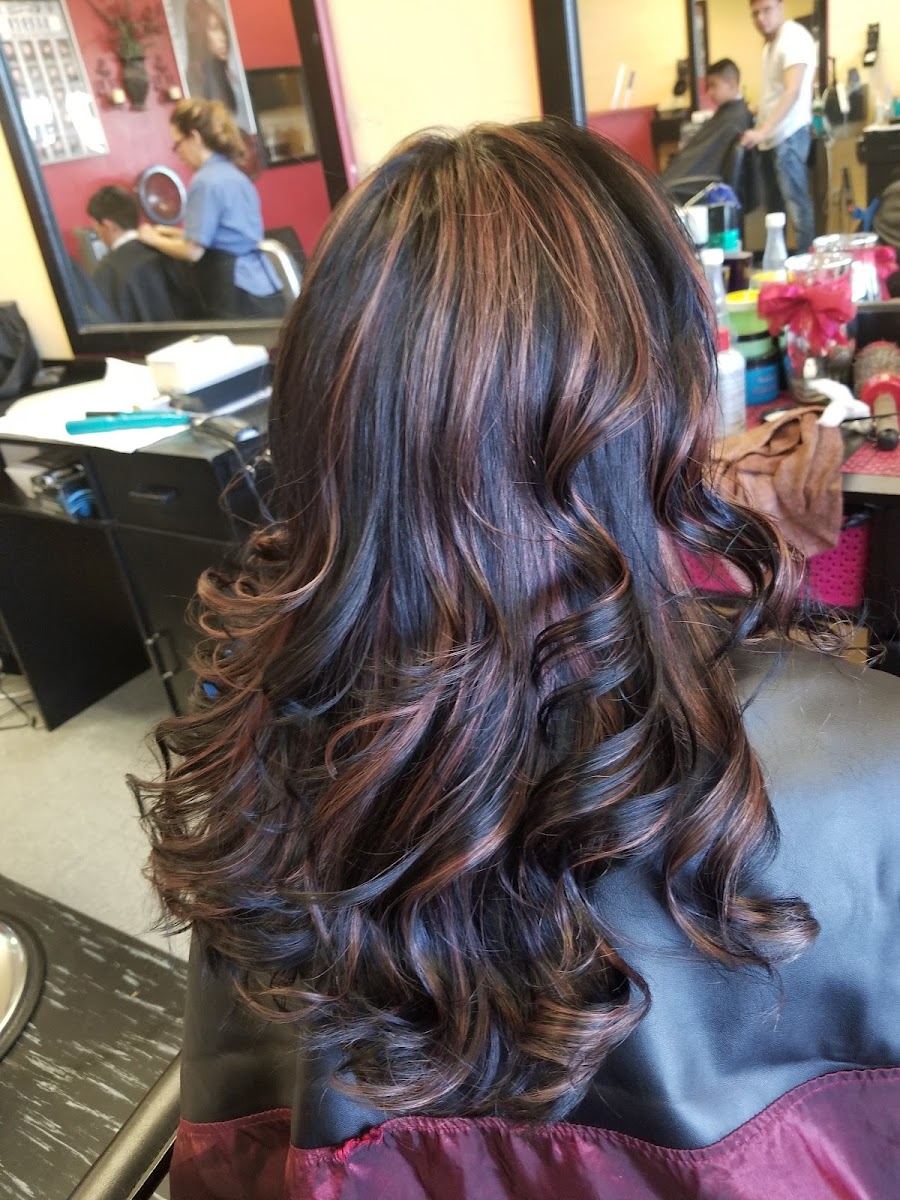 Long dark hair with warm copper highlights and soft curls, styled at La Tijera Magica