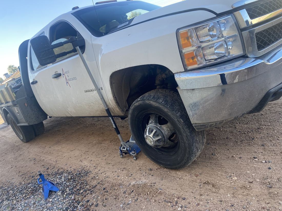 White pickup truck raised on a floor jack with the front wheel removed