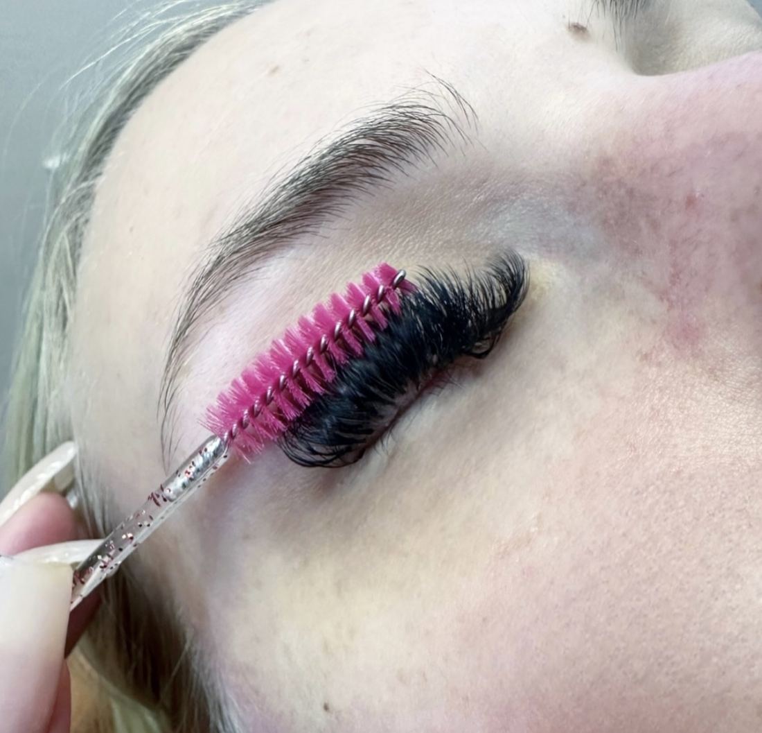 A pink spoolie brushing through a full set of dark lashes