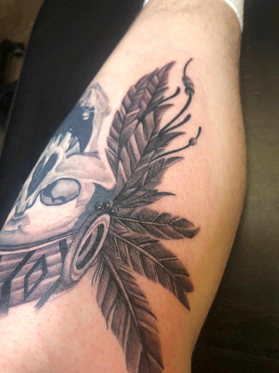 Black and grey tattoo of a skull with beaded feathers