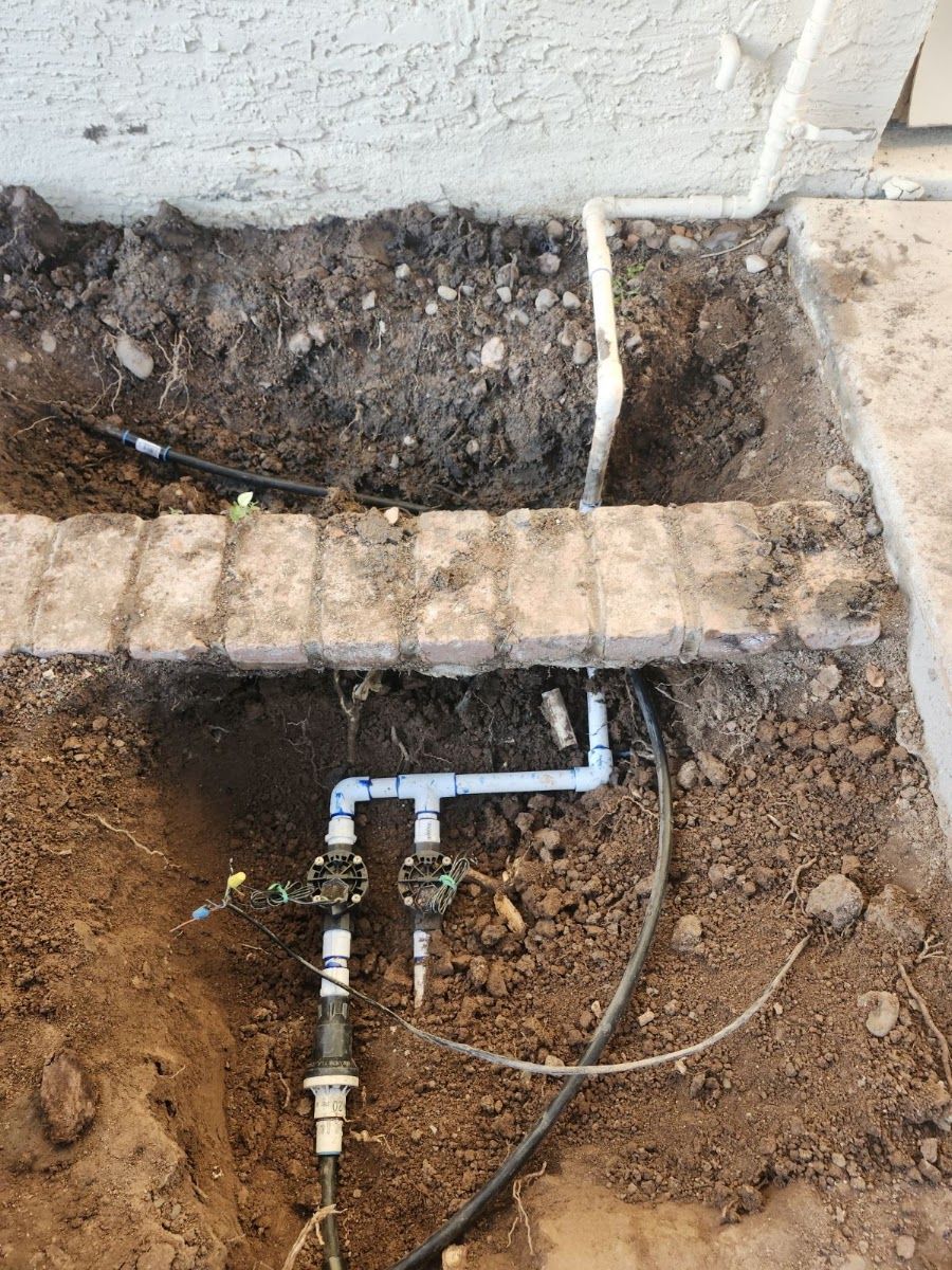Irrigation line and valve exposed in a dug trench beside a brick border
