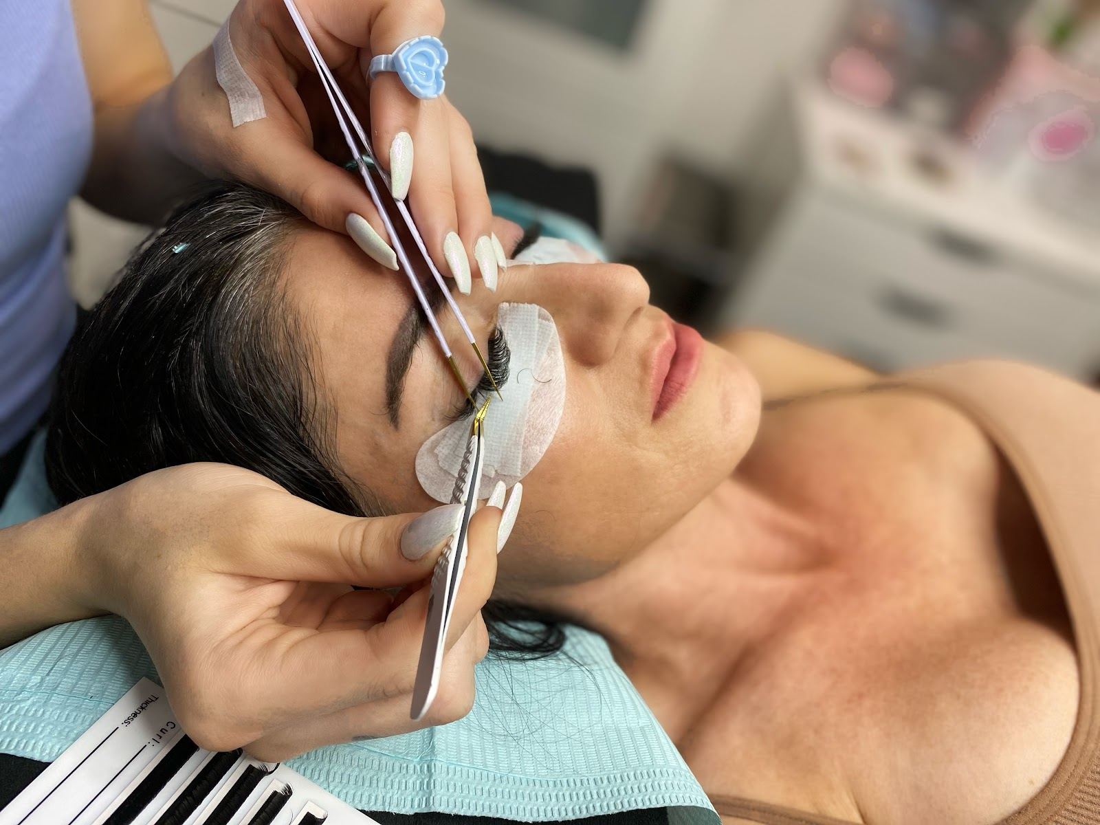 Lash extensions being applied with tweezers to a client lying back on the treatment bed