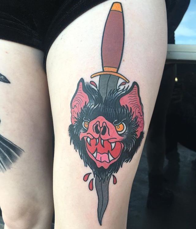 Traditional style bat head pierced by a dagger tattooed on a thigh