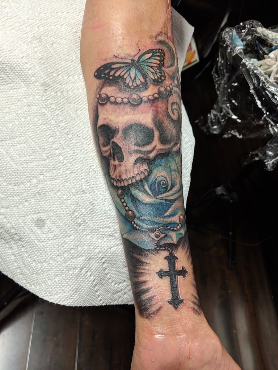 Skull, butterfly, rose and rosary tattoo on a forearm