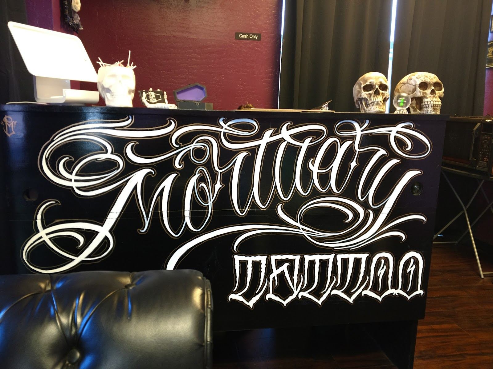 The Mortuary Tattoo front desk lettering in white script with two skulls on top