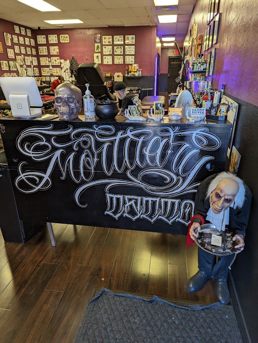 Inside Mortuary Tattoo: the front desk with the shop name in script lettering, flash art on the walls