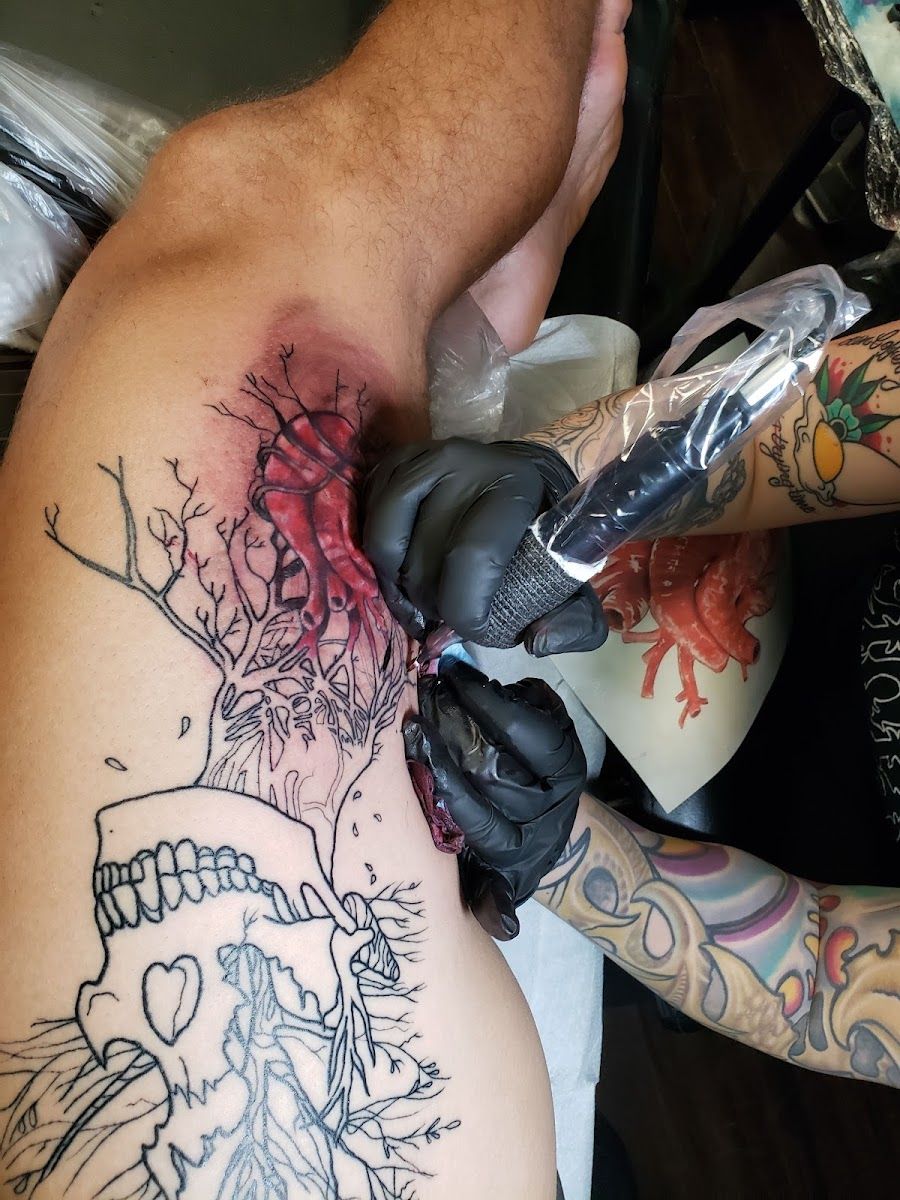 An artist in black gloves working on a skull tattoo