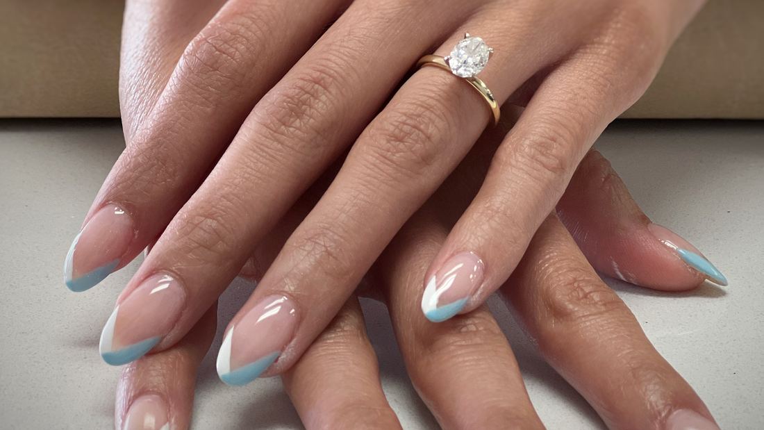Almond nails in sheer nude with thin light blue French tips and a diamond ring