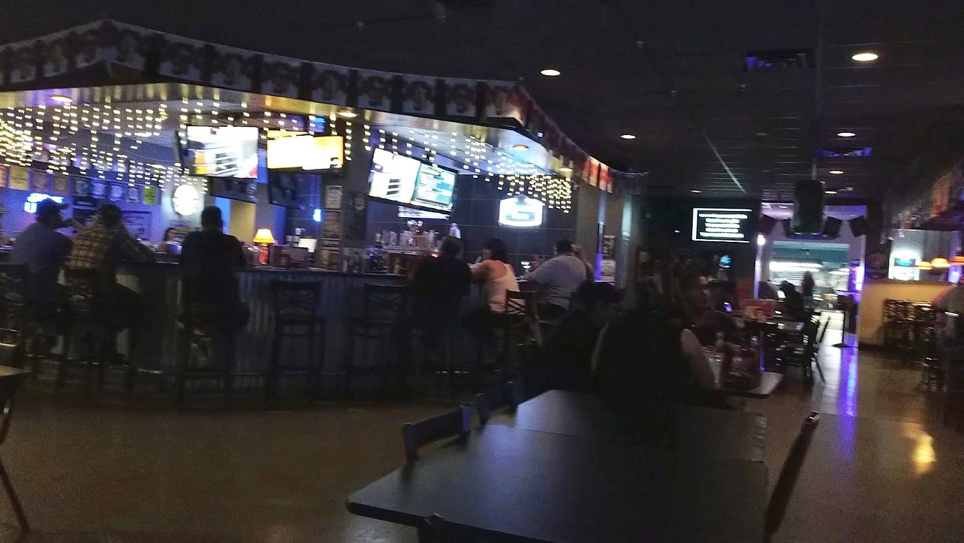 The bar at night: string lights, TVs and neon signs over a long bar with people seated along it