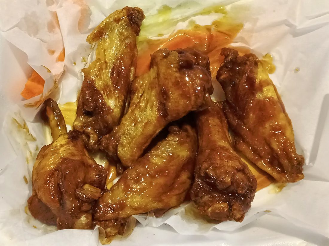 A basket of glazed chicken wings on paper with carrot sticks