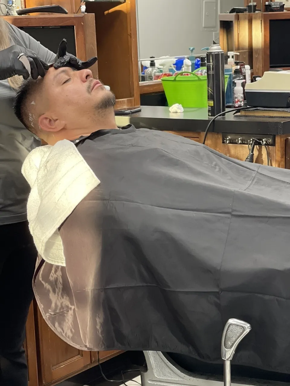 A client leaning back in a barber chair under a black cape for a shave