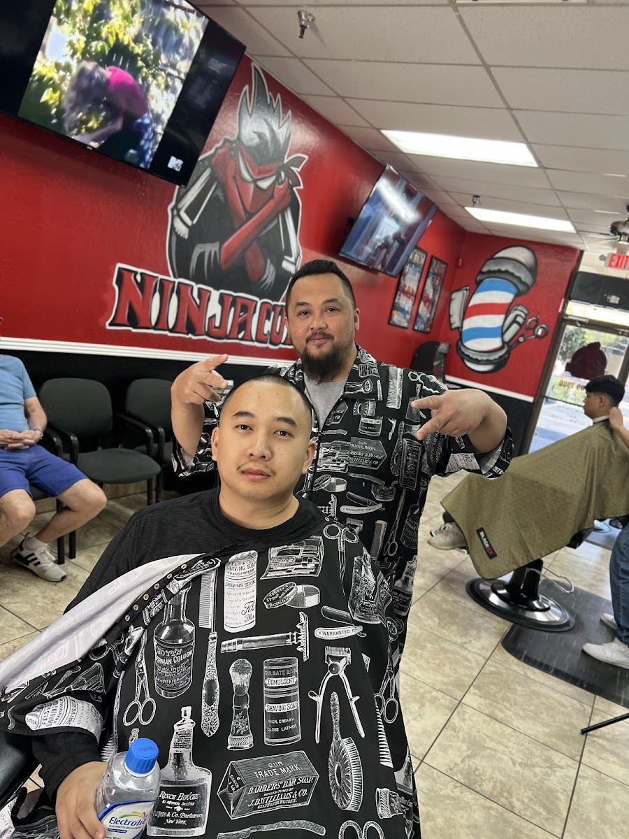 A Ninja Cuts barber and a client posing in front of the shop's red ninja wall mural
