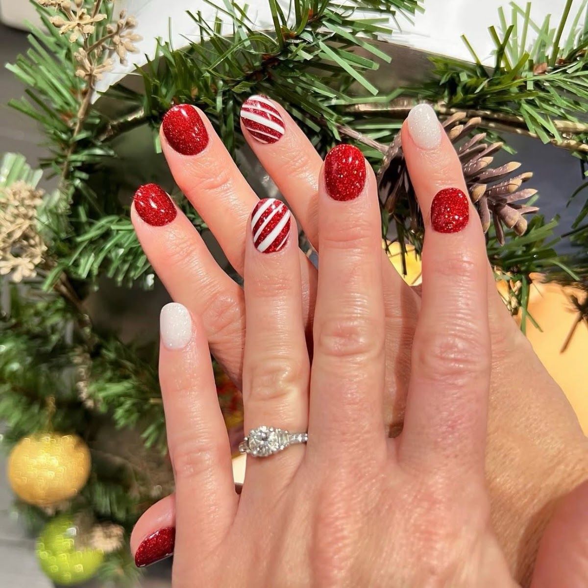 Red glitter and candy stripe nails beside a pine garland