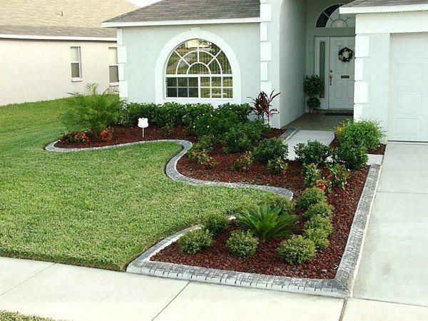Curved flower bed with shrubs and red mulch edging a front lawn