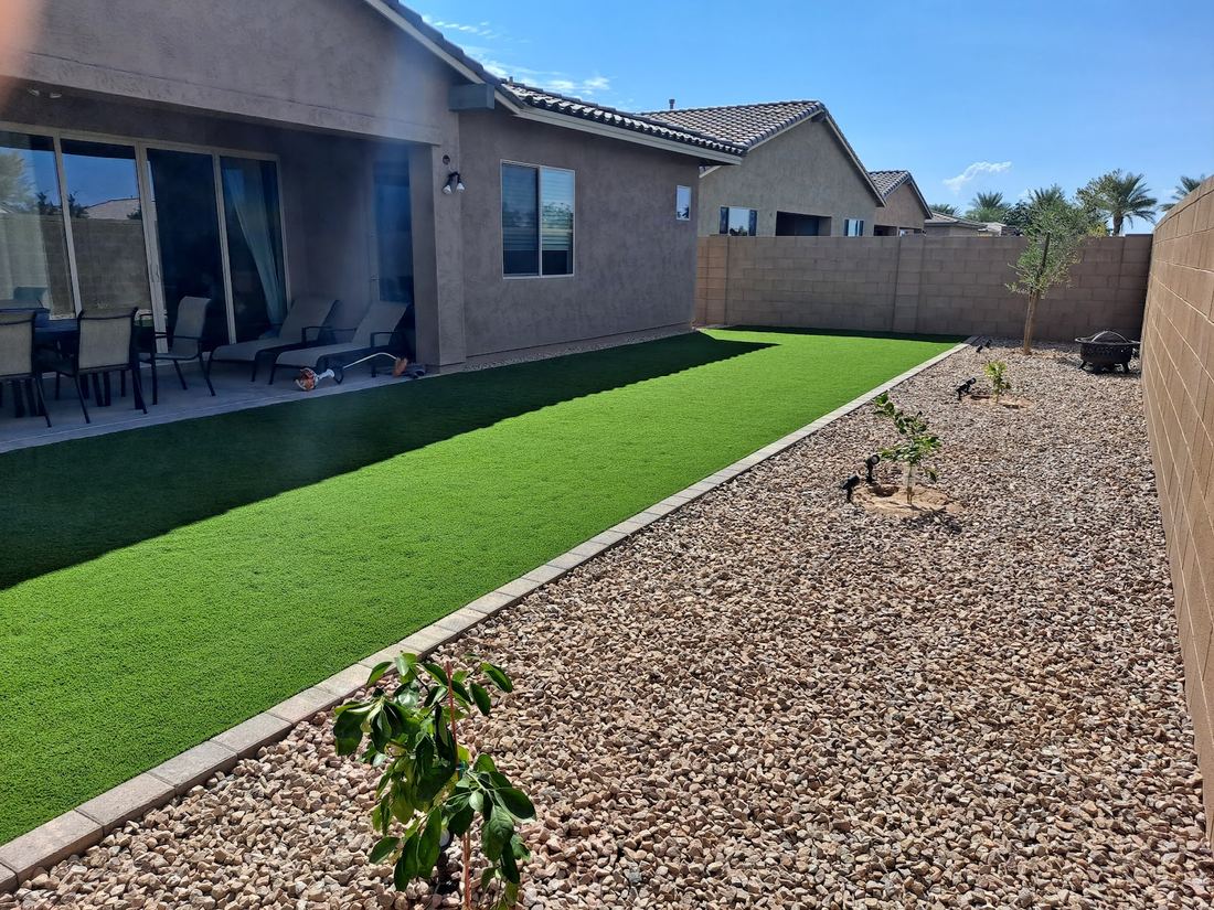 Backyard strip of bright green turf beside a decorative rock bed