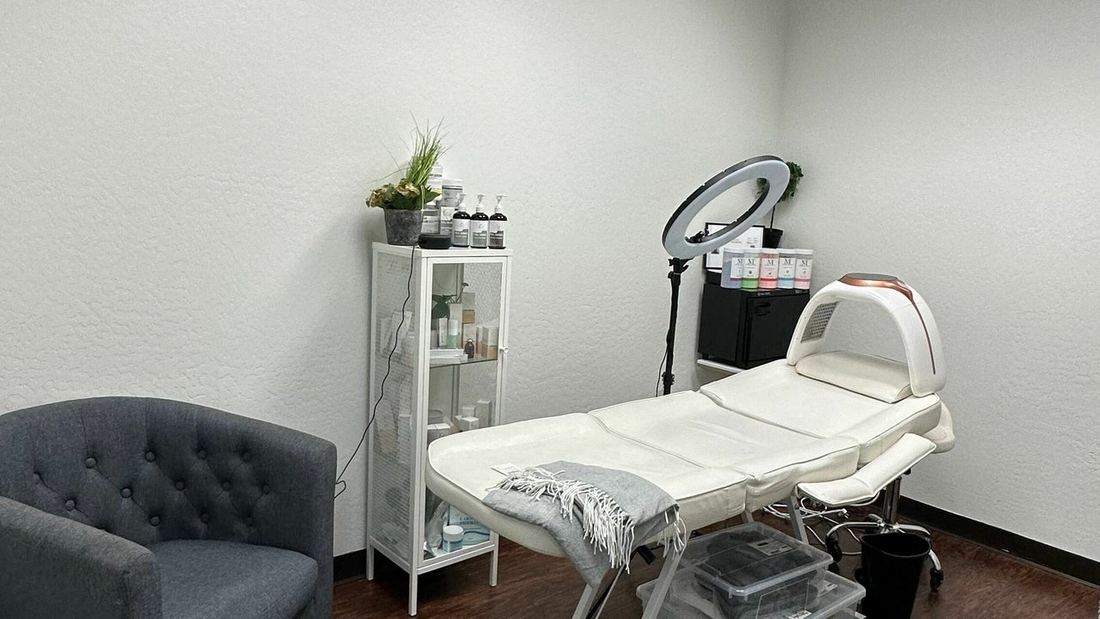 The treatment room with a white treatment bed, ring light and grey armchair