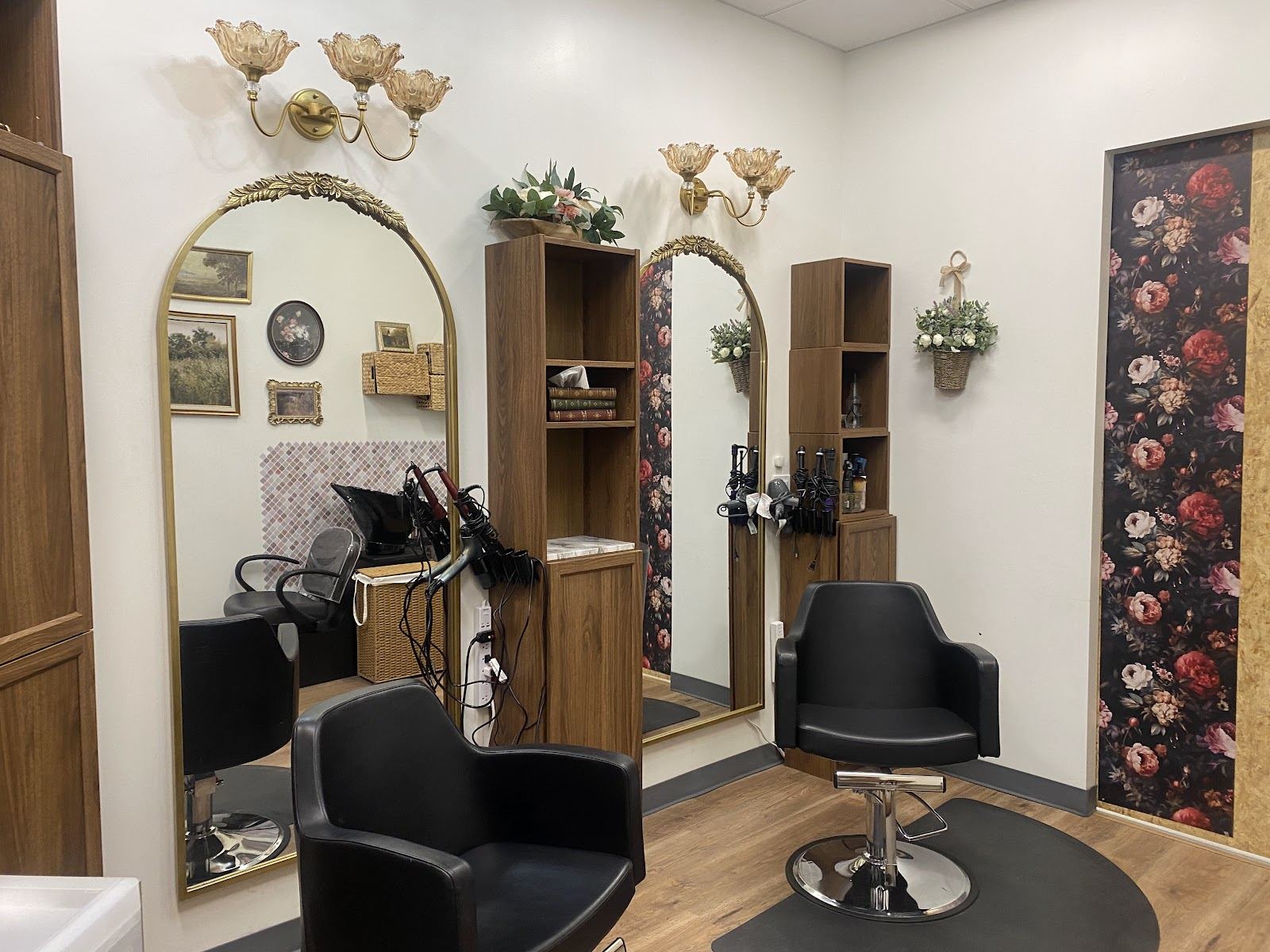 Inside Personalities Salon: black styling chairs, gold arched mirrors, brass flower sconces and a dark floral wallpaper panel