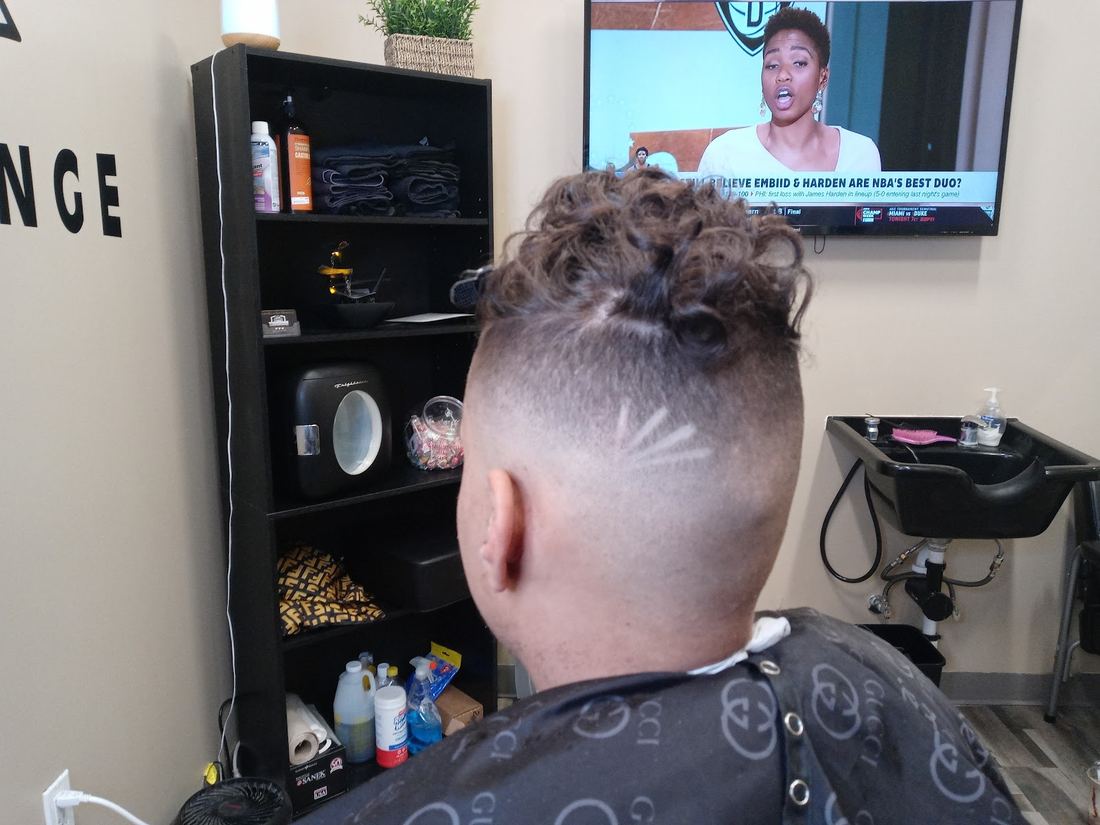 Inside the lounge: a client with a curly top and a fresh fade, shelves and a TV behind