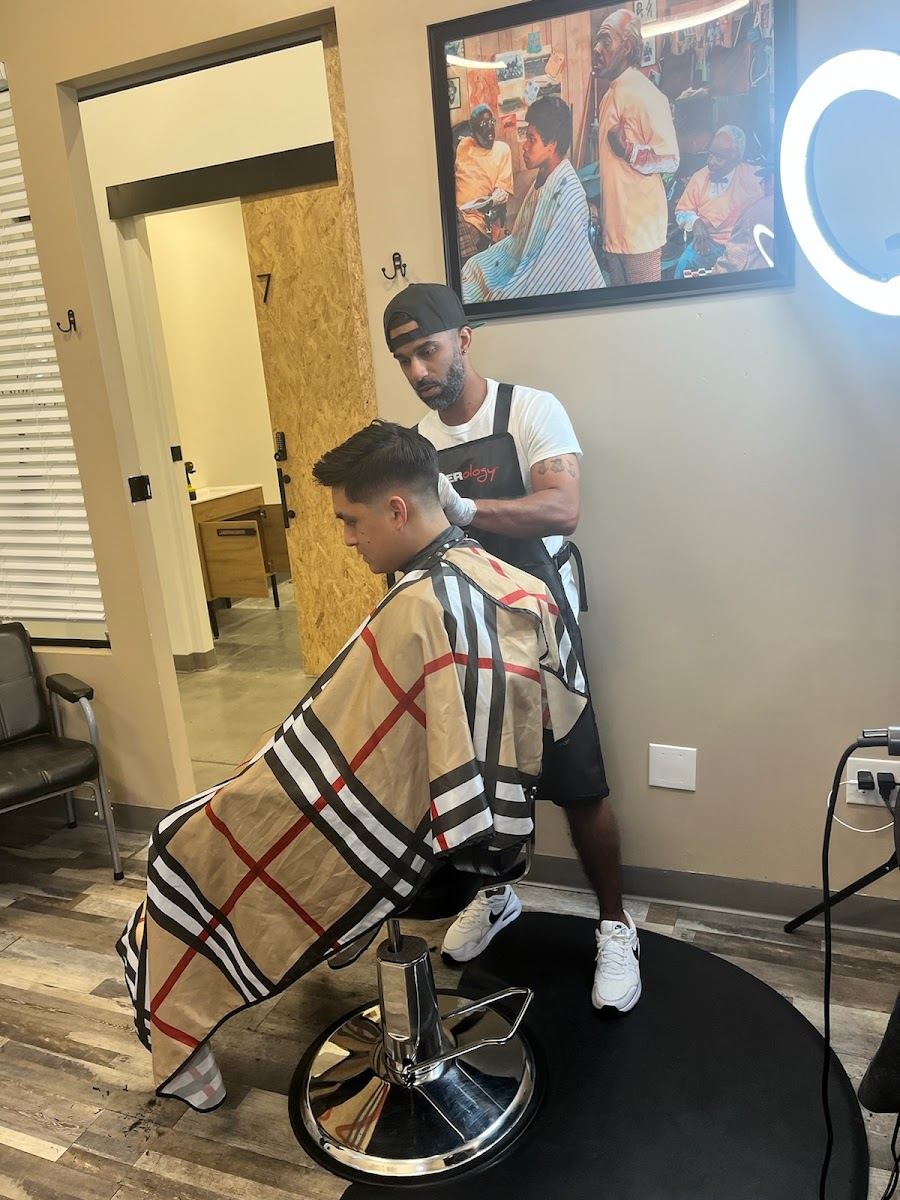Barber at work on a client in a plaid cape inside the Quality Cutz lounge