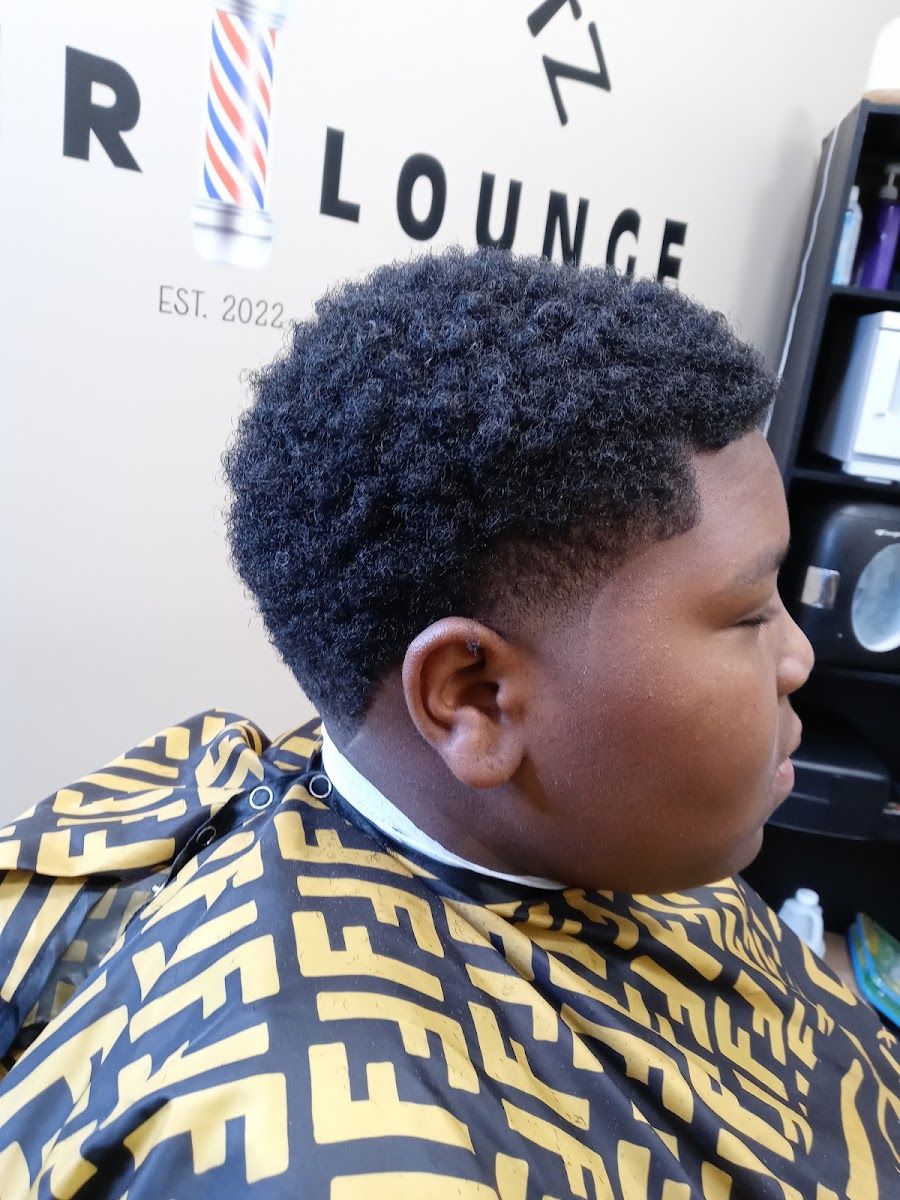 Young client with a curly top and a clean taper under the lounge sign