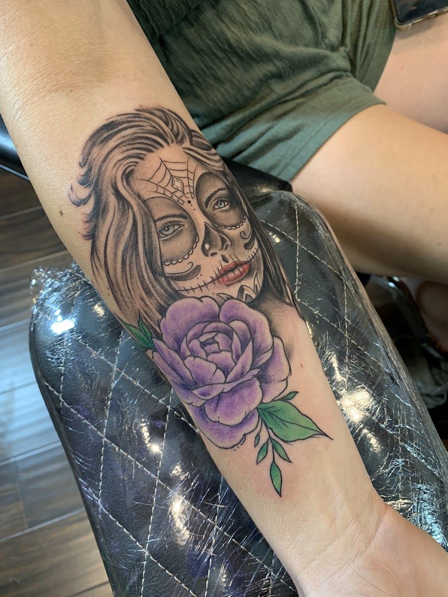 Sugar skull woman portrait tattoo with a purple rose on a forearm