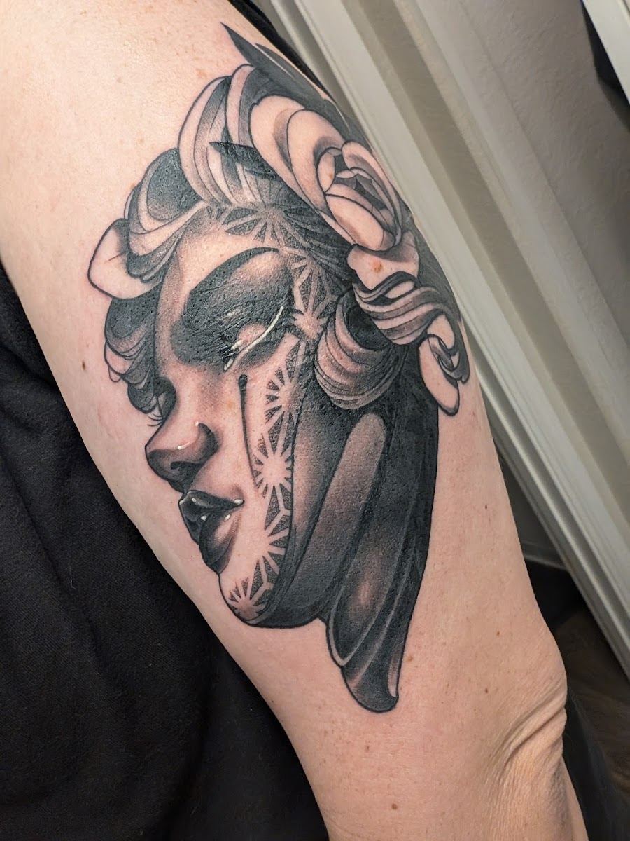 Black and grey tattoo of a woman's face framed by roses on an upper arm