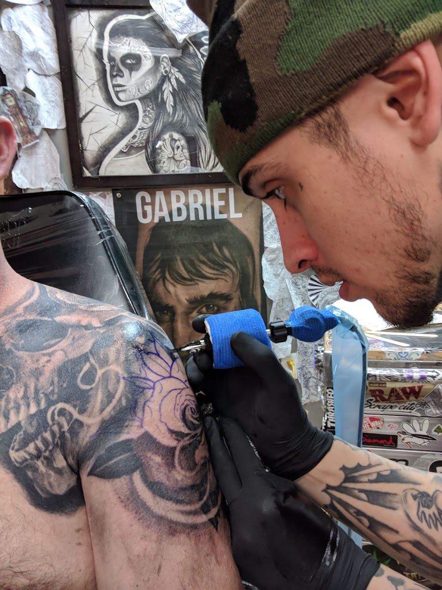 An artist at Royal Craft Gallery tattooing a black and grey rose over a skull shoulder piece