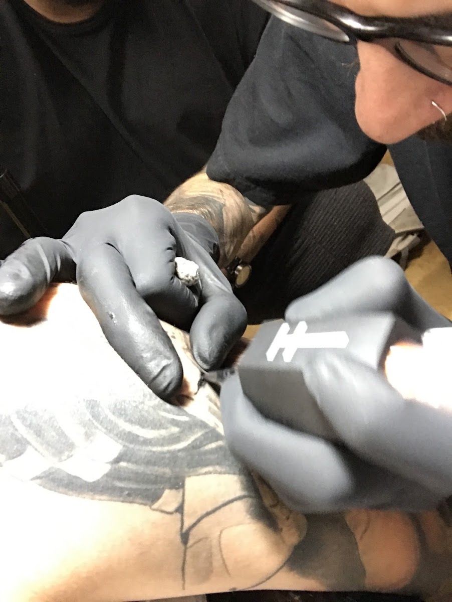 Gloved hands shading a black and grey tattoo in progress