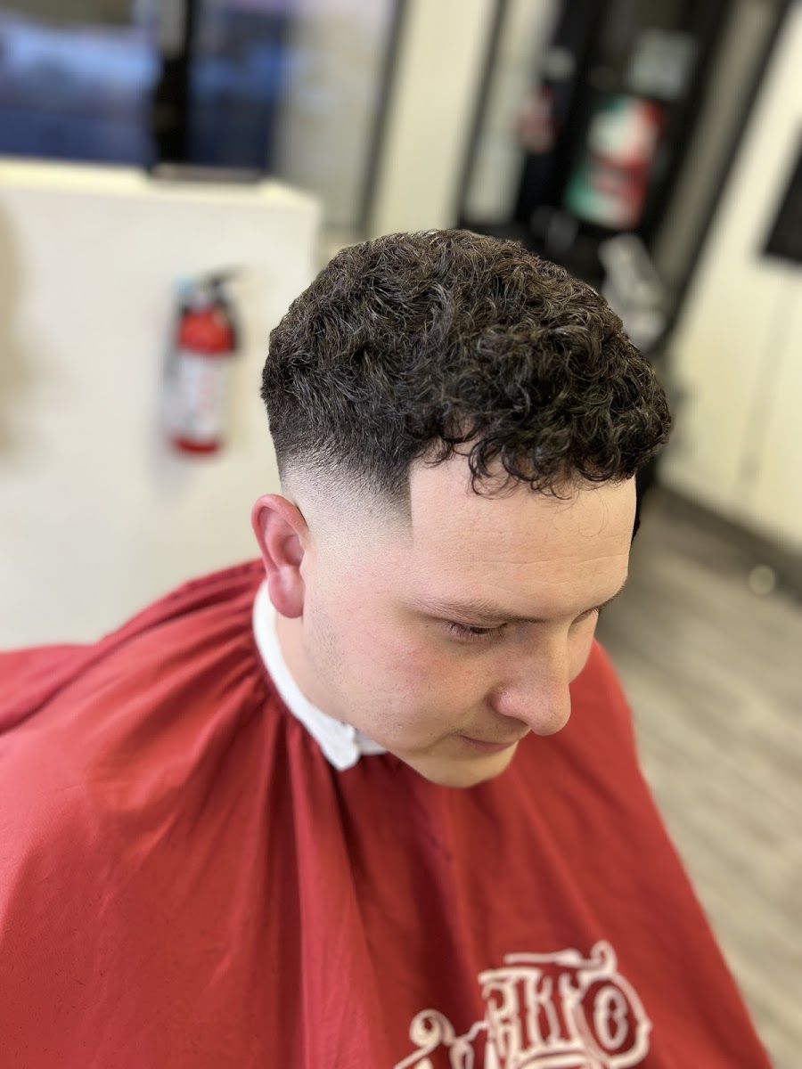 Curly top with a taper fade on a client in a red cape