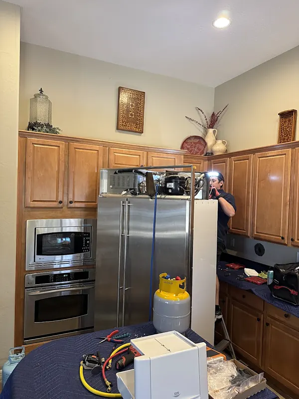 Stainless refrigerator in a kitchen with wood cabinets, a yellow tank and tools set in front of it