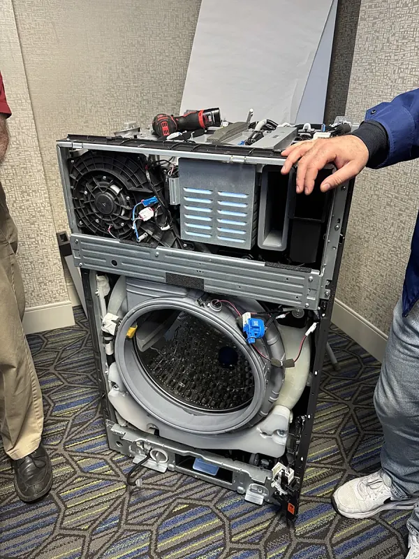 Front-load washer with its top panel removed, a hand resting on the frame