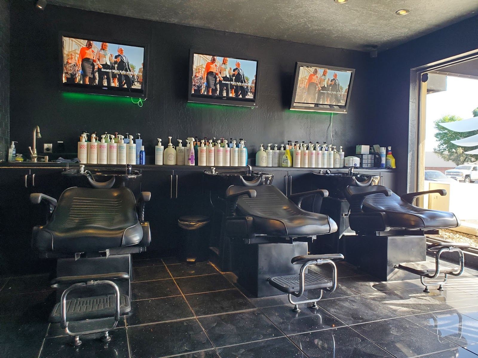 Three black shampoo chairs under green-lit screens inside Saints & Scissors Salon