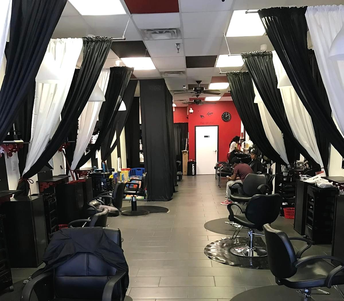 Inside the salon: black and white curtains between stations, black chairs and a red back wall