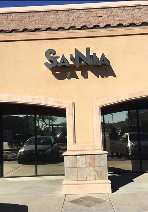 Tan stucco storefront with dark SA'NIA letters above arched windows