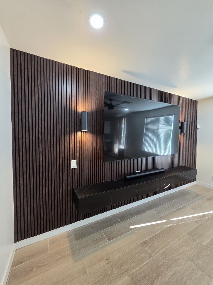 Dark wood slat accent wall with mounted TV, wall sconces and a floating media console