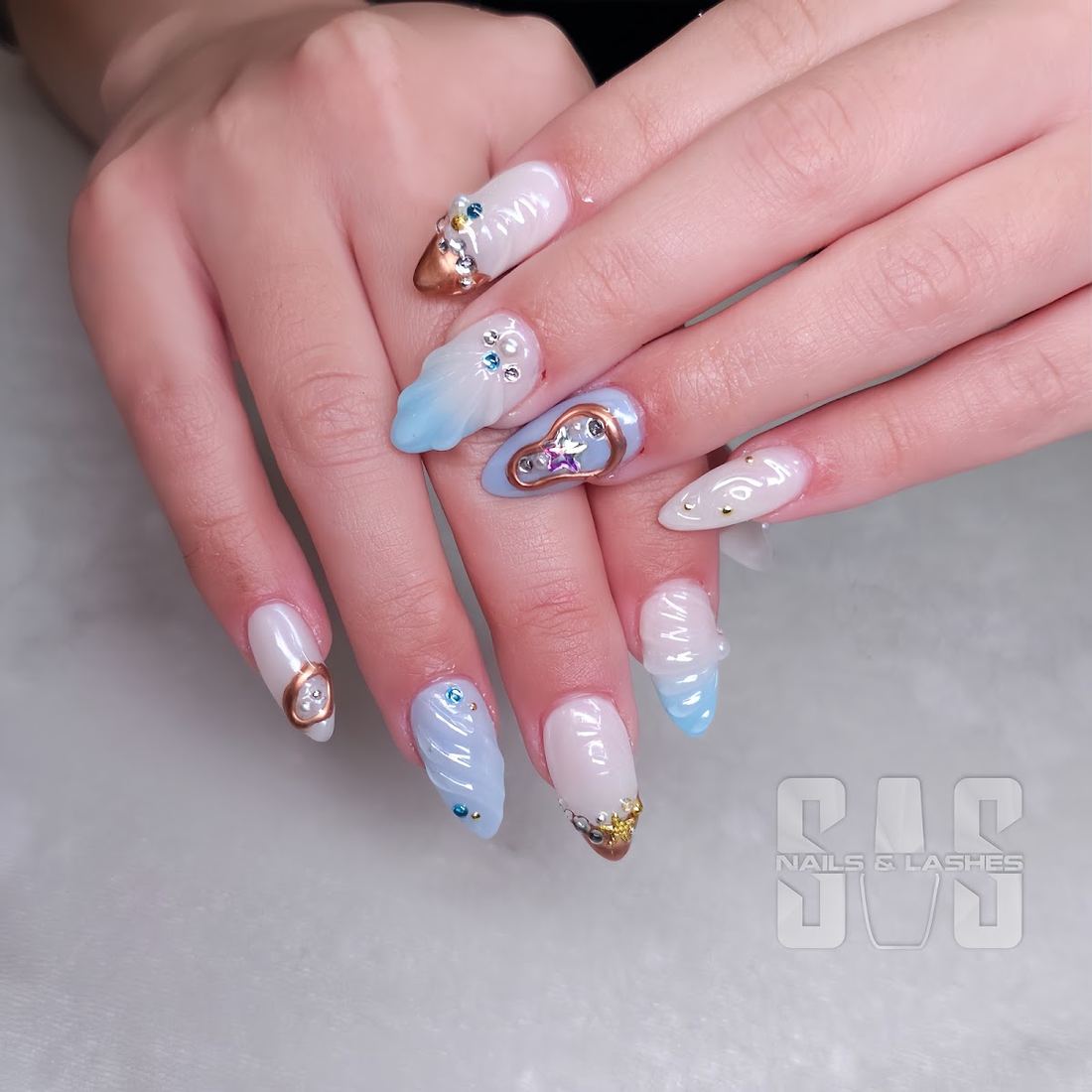 White almond nails with blue swirls and gold charm accents