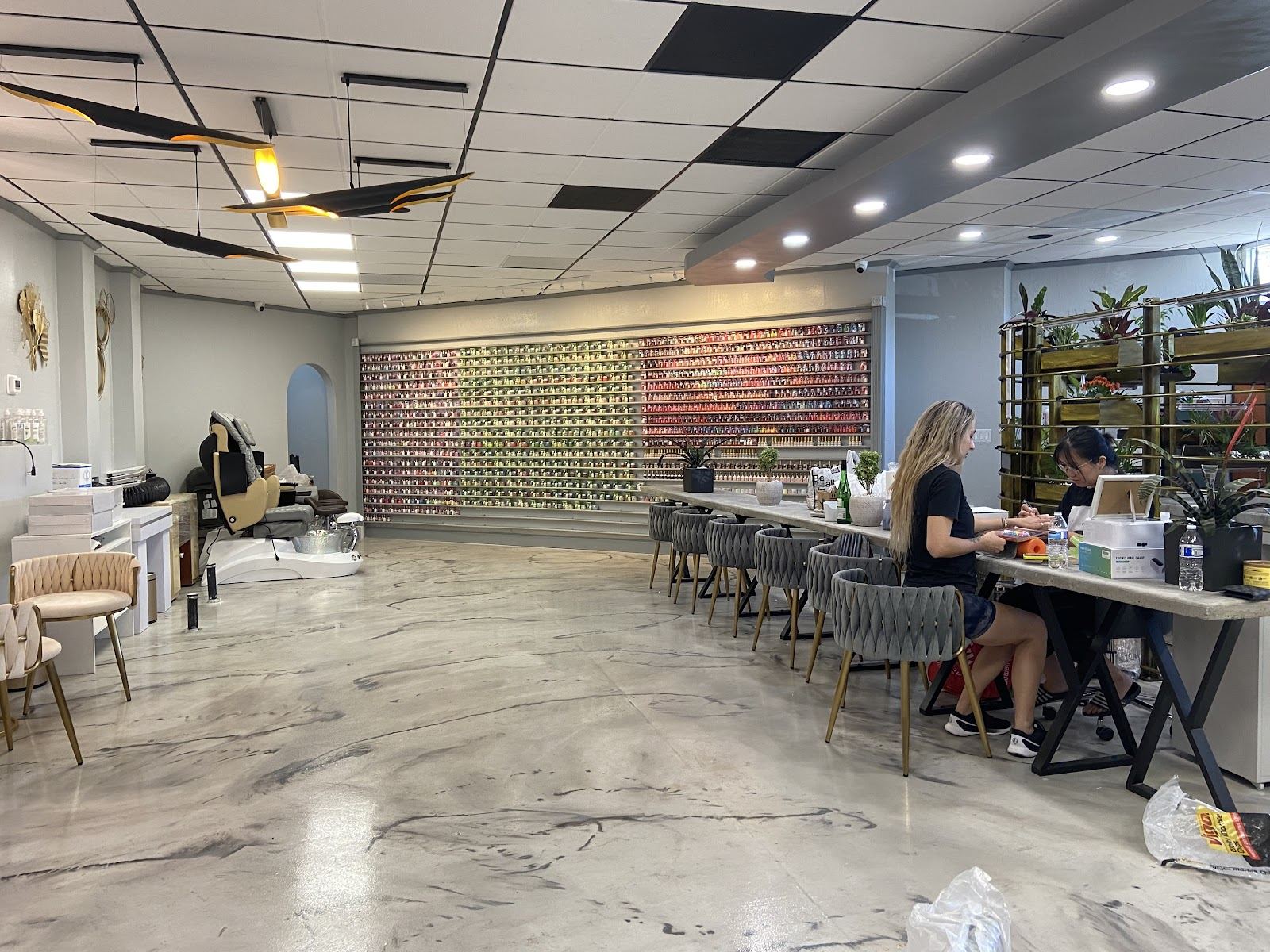 Inside SIS Nails & Lashes: a long bright room with a full wall of polish colors and manicure stations