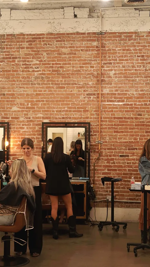 The salon floor: an exposed red brick wall, black framed mirrors and stylists at work