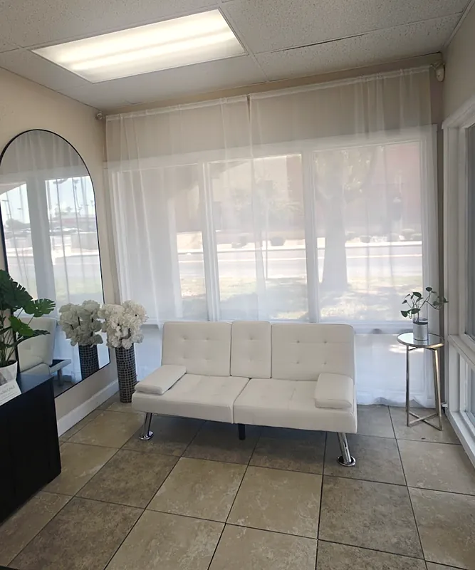 A bright waiting area with a white sofa, sheer curtains and an arched mirror