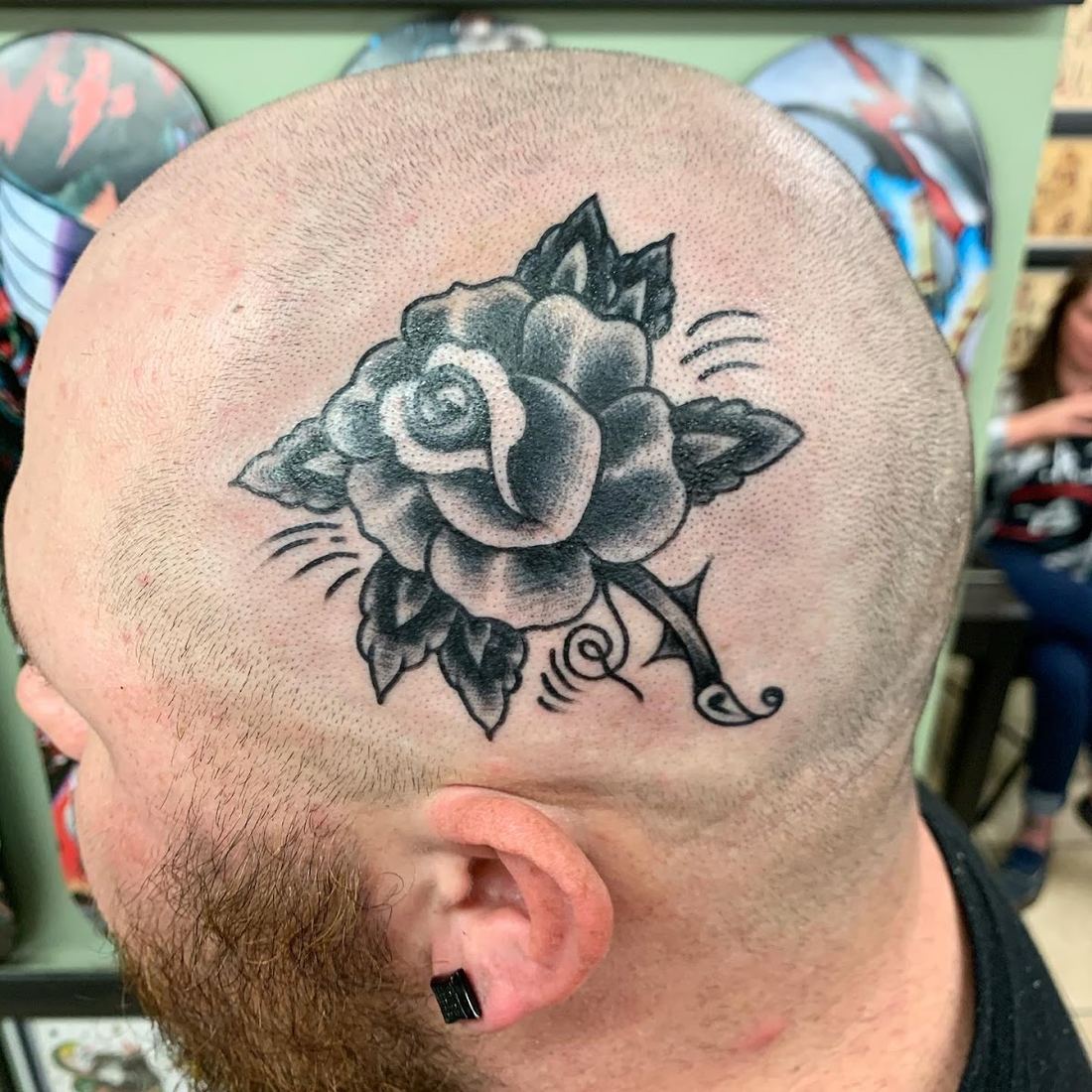 Black and grey rose tattoo on the side of a shaved head