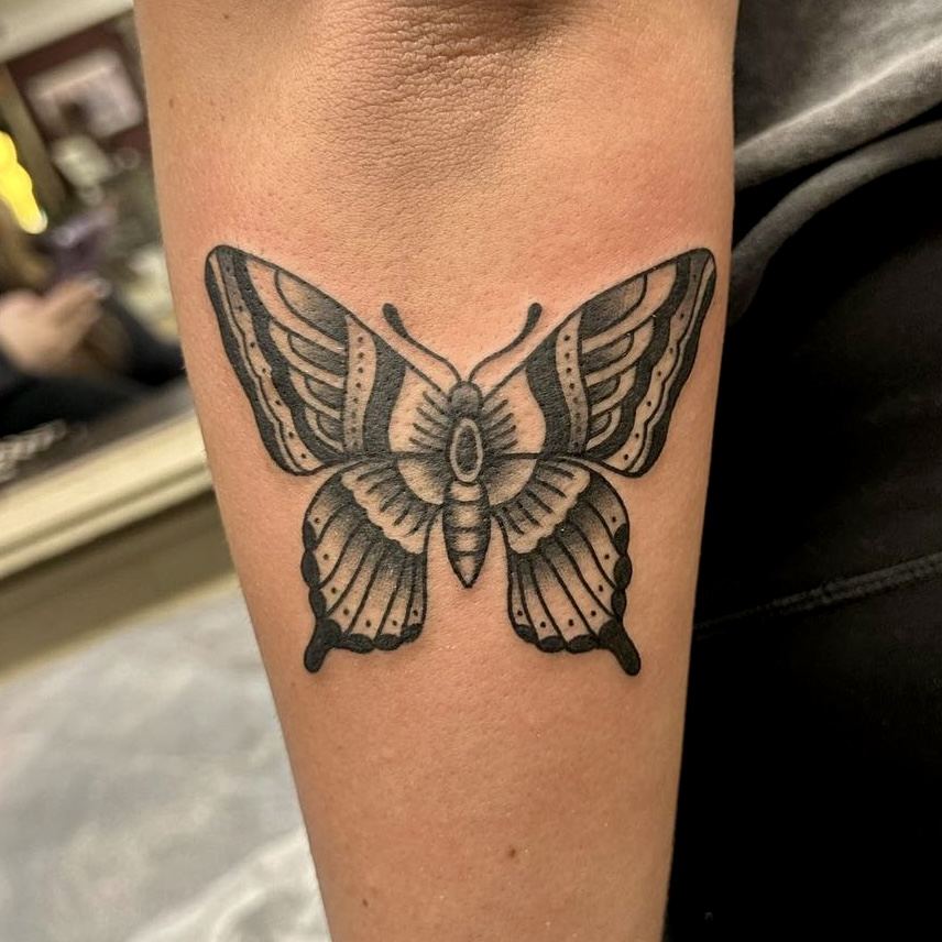 Black linework butterfly tattoo on a forearm