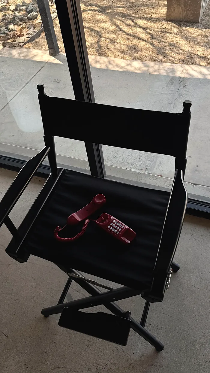 A black director's chair with a red phone resting on the seat, by a window.