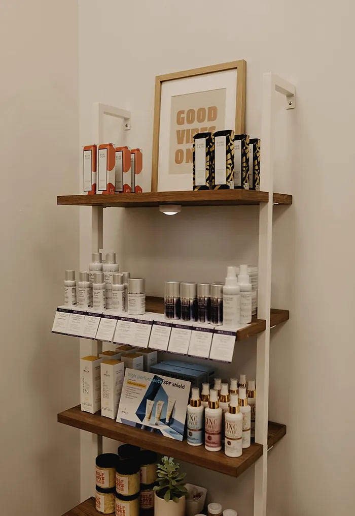 Wall shelves of skincare bottles under a framed good vibes only print.