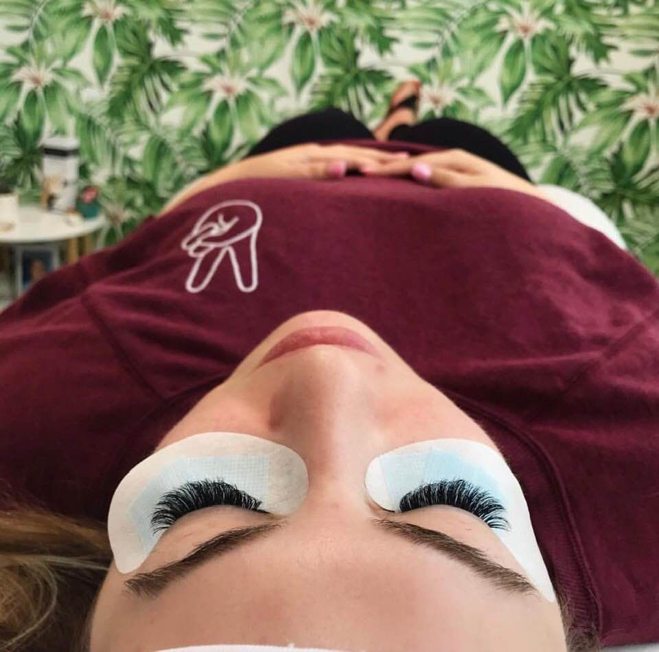 A client resting with lash extensions in front of the studio's monstera wallpaper