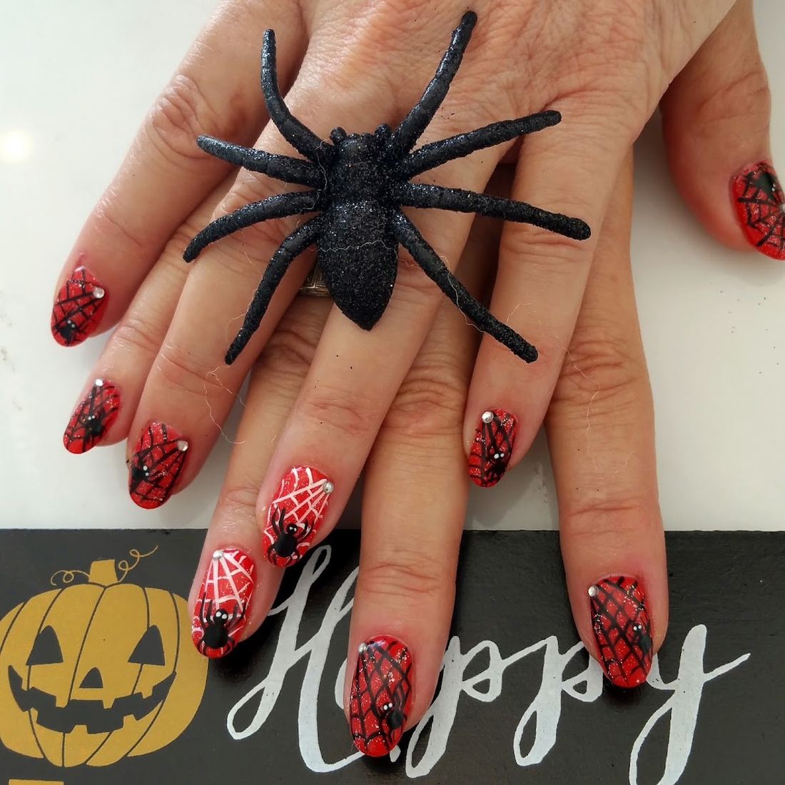 Red nails with black spiderweb art beside a glittery toy spider